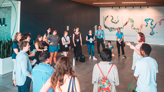 A group of Bonner scholars stand in a group in a musuem listening to a speaker. A large abstract painting is prominent in the background.