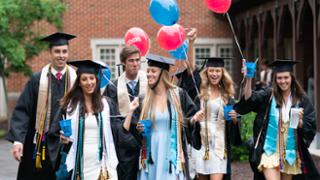 Seniors wearing their caps and gowns and holding red and blue balloons as they participate in the senior walk to the commencement ceremony.