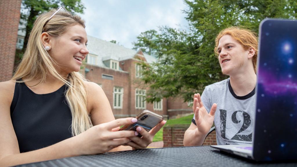 Two students sitting at a table and having a conversation outside.