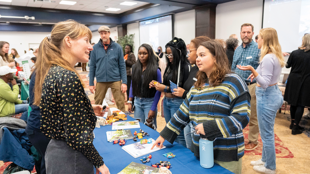 a group of students speaking to a woman at a table and looking at the materials on the table