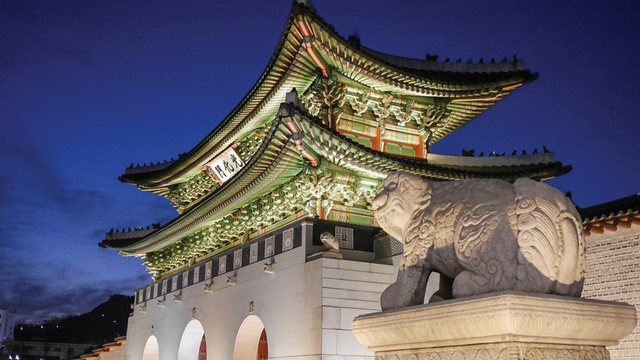 an statue in front of a korean style building lit in the night