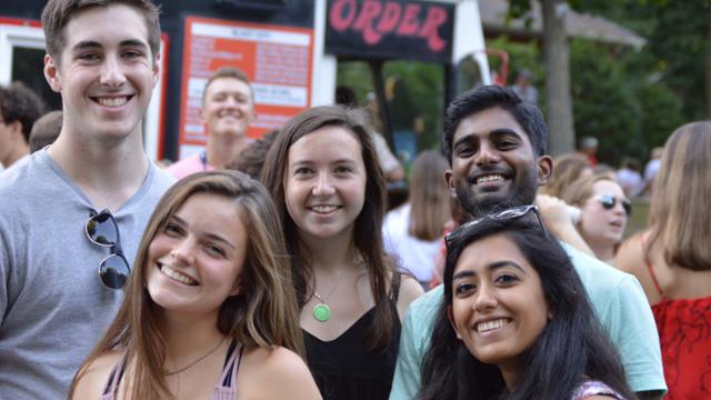 Group of students attending an outdoor CSI event with food trucks.