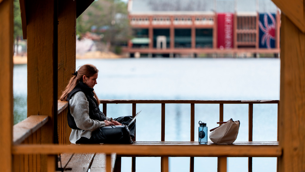 A student with a laptop in the gazebo on Boatwright Lake