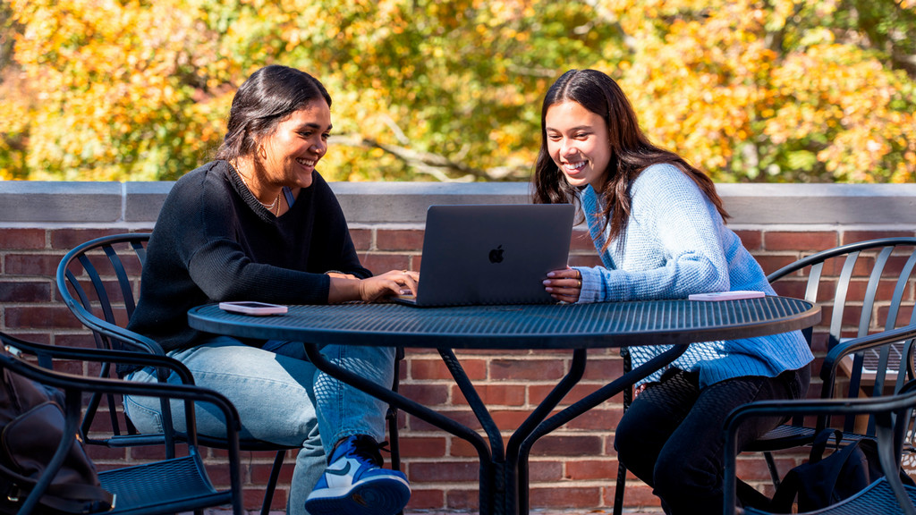 Two students with laptops outside in the Fall