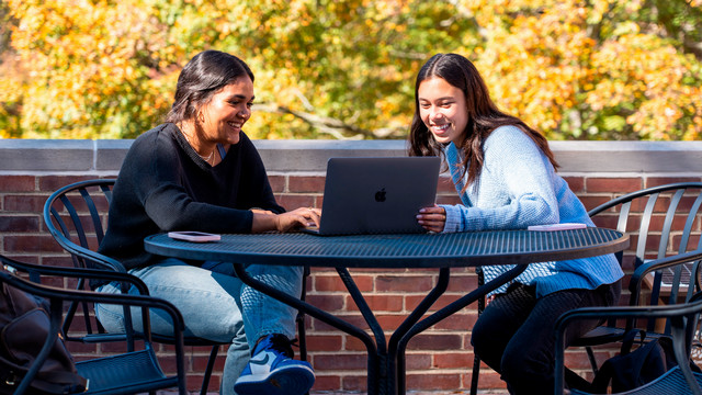 Two students with laptops outside in the Fall