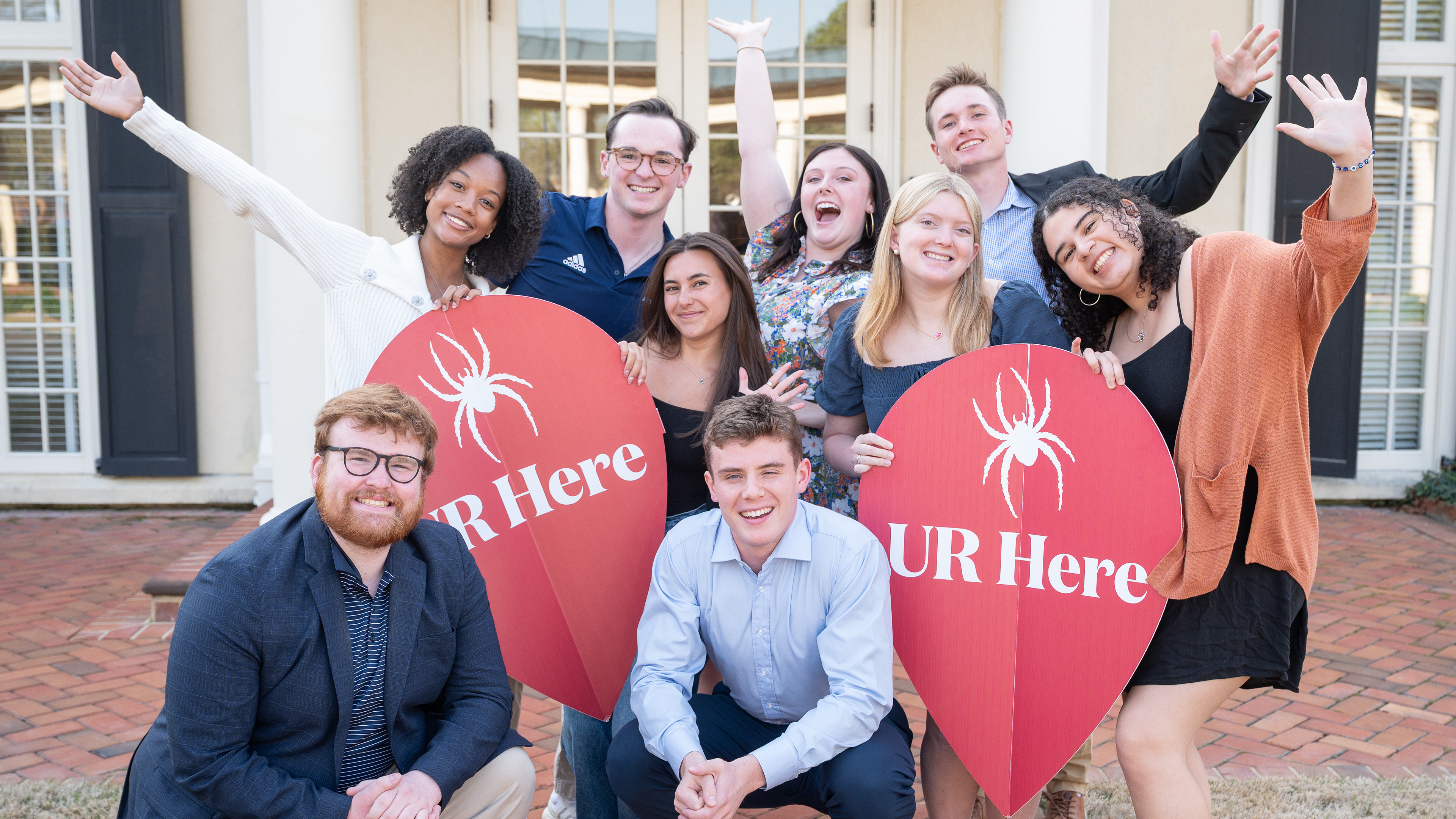 A photo of Jepson students posing with large red map pin UR Here logos. They are holding up their hands and smiling into the camera.