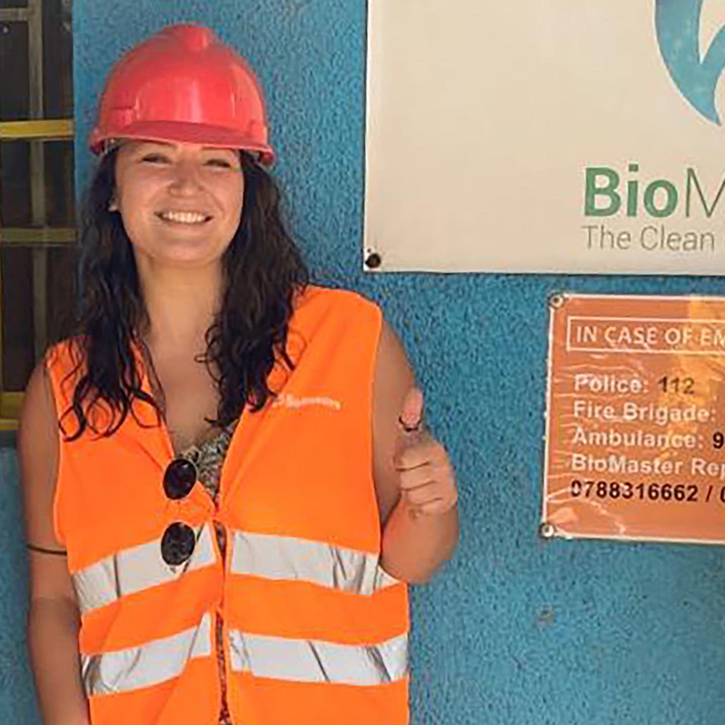 An environmental portrait of Yasmine Karam wearing a high-vis vest and an orange hard hat.