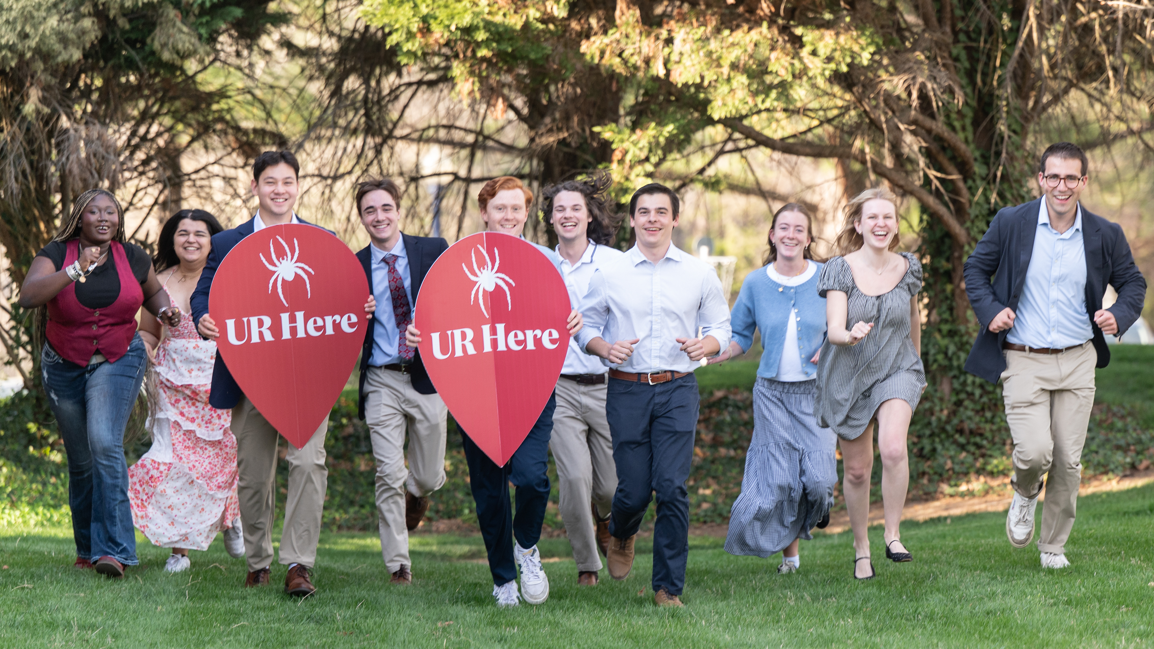 A photo of Jepson students posing with large red map pin UR Here logos. They are holding up their hands and smiling into the camera.