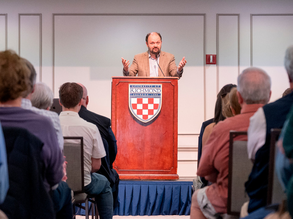Ross Douthat standing at a podium and gesticulating at his talk at the McDowell Institute at the Jespon School of Leadership Studies at the University of Richmond.