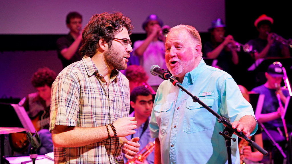 two men sing with a big band backing them
