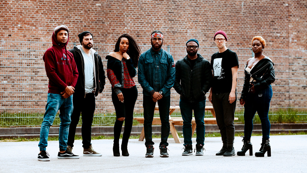 Cory Henry & the Funk Apostles stand together in front of a brick wall
