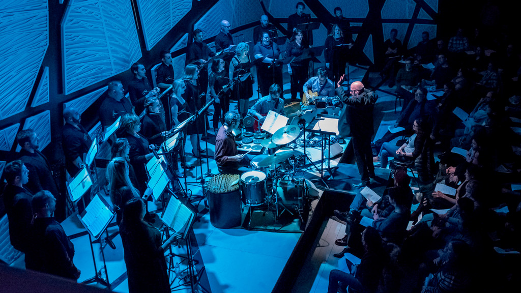 conductor leads an instrument ensemble and singers performing together on stage