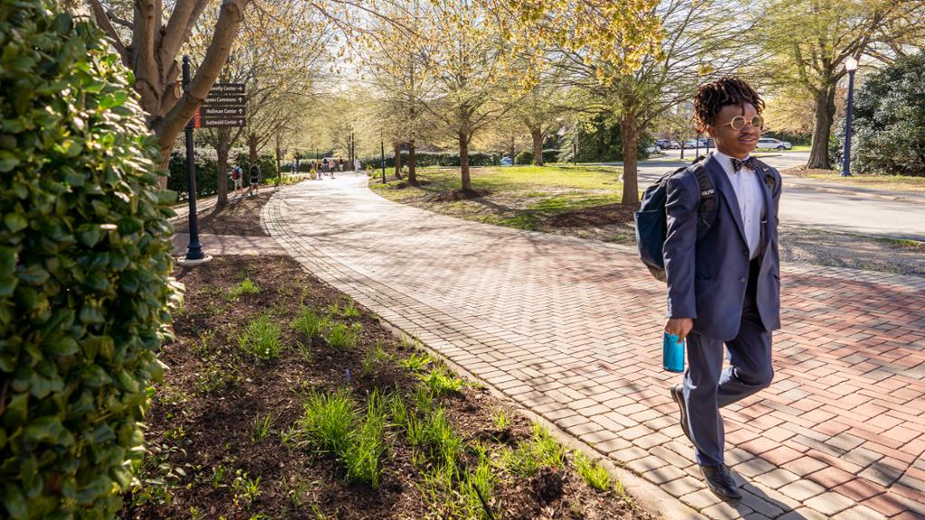 A student in a suit walks along a brick path.