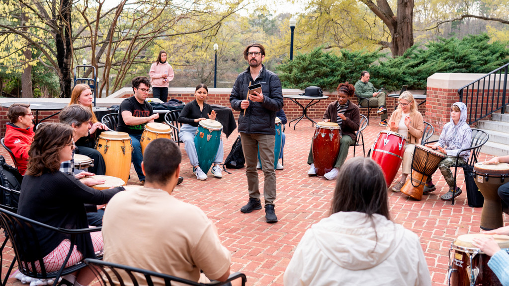 A class meets outside on the library patio to participate in a group drum circle.