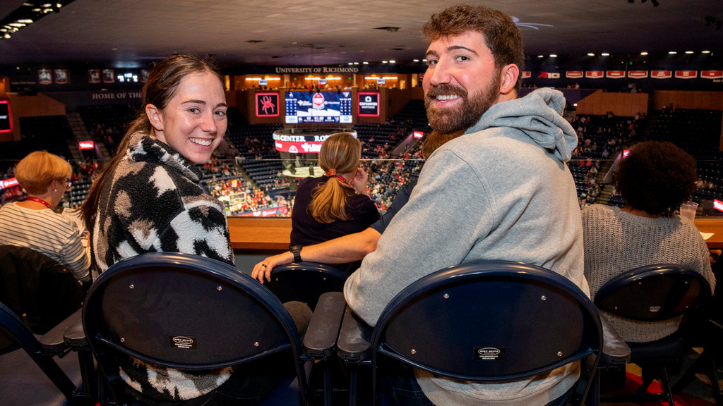 Two seated people watching a basketball game, turned toward the camera for a photo