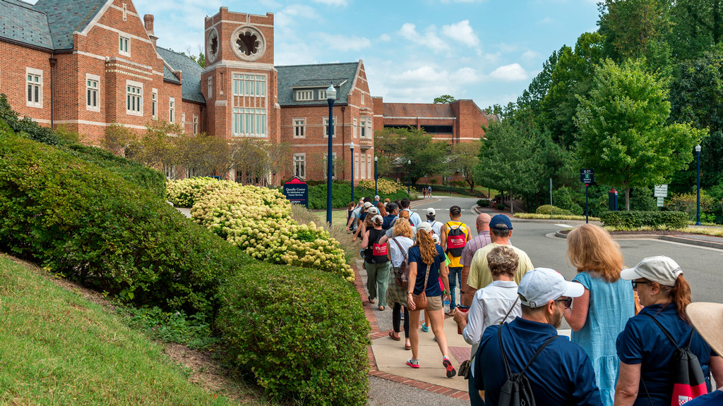 A line of people on a tour walking toward a large brick building