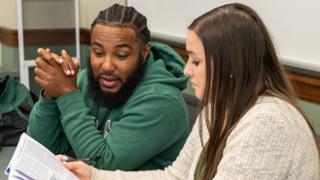 Two students talking about an article one is holding