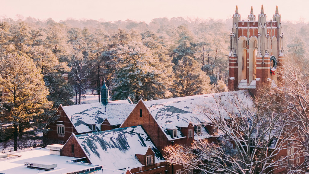 Snow-covered roofs and brick tower with a background of fog-covered trees at sunrise