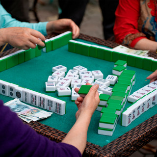 Multiple players engaged in a mahjong game on a turquoise playing surface with white tiles featuring Chinese characters, green tile racks, and currency visible, demonstrating traditional Asian tile-based gameplay.