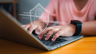 Person typing on laptop keyboard with security icons overlaid