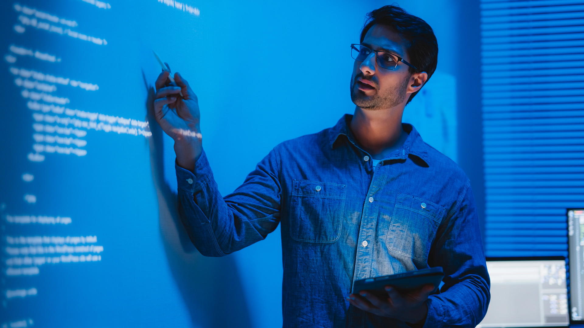 Teacher in front of a projection of computer code pointing to the screen