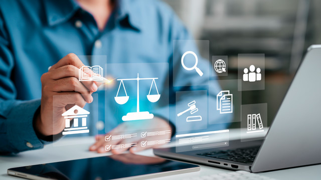 A close-up of a person using a stylus on a digital screen displaying legal-themed icons, including the scales of justice, a gavel, a law book, and a courthouse, with a laptop visible in the foreground.