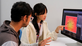 Two students work together using photoshop at a large computer screen.