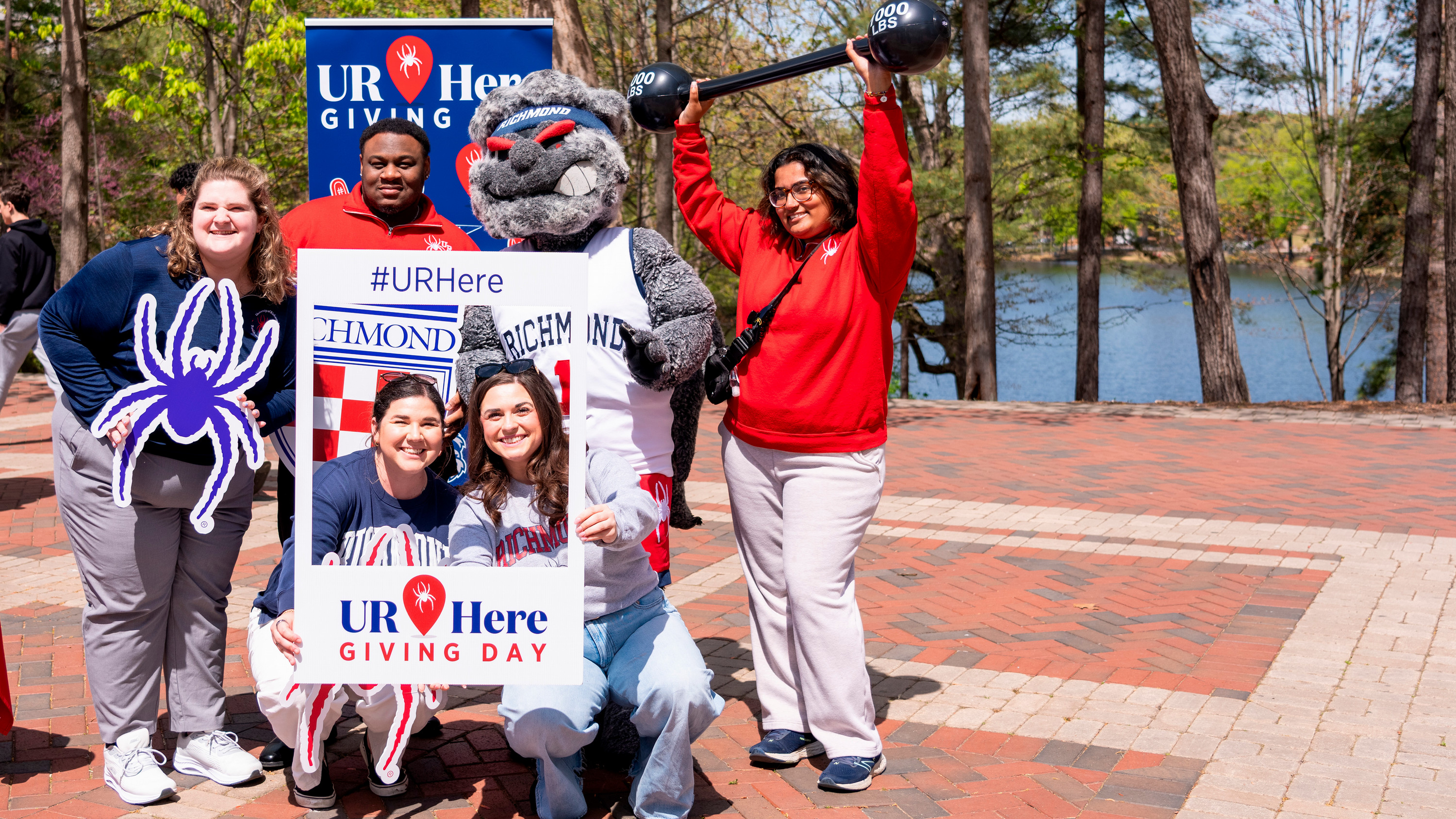 A group of students posing on the forum with photo props to promote UR Here giving day.