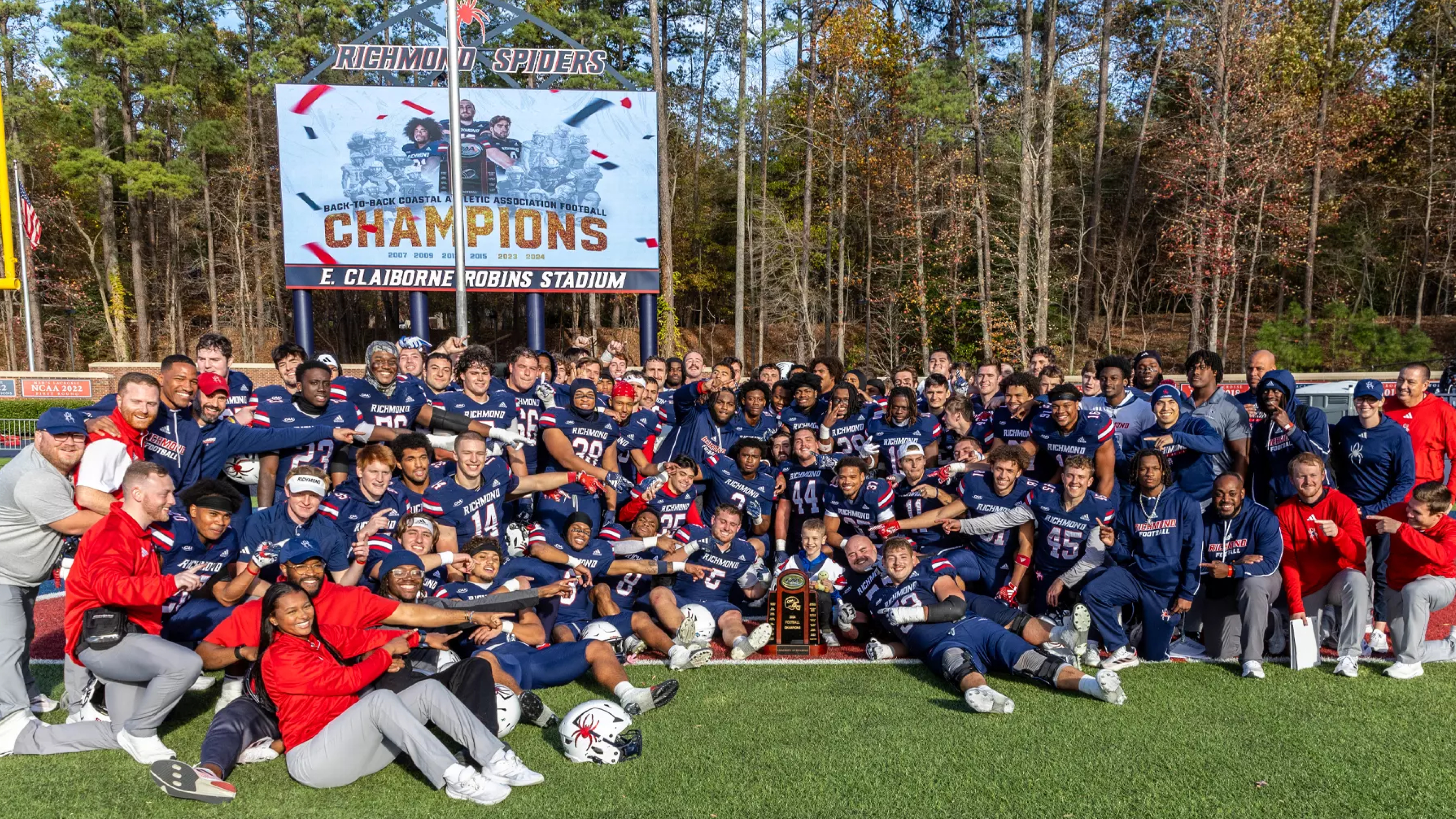 University of Richmond football tram posing on the field at Robins stadium with the Capital Cup trophy.