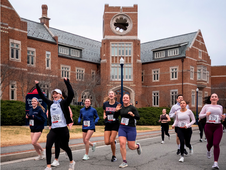 A group of Spider Dash 5k participants in front of Queally hall at the university of Richmond. They are smiling for the camera, and one runner is raising her arms victoriously.