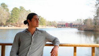 A photo of Ibrahim Alkaseer on campus at the gazebo with Westhampton Lake, and the commons in the background.